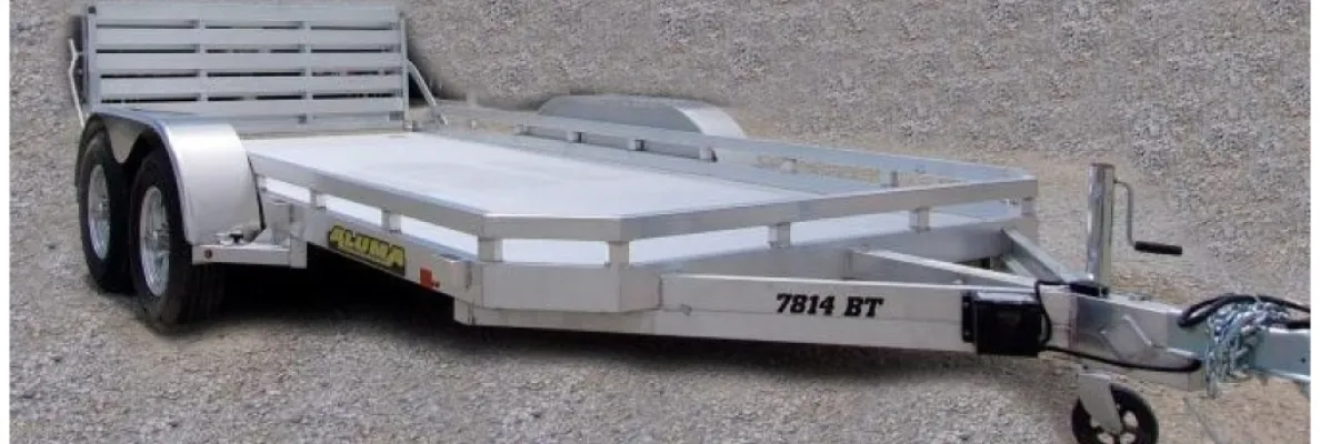 Aluminum utility trailer with dual axles on gravel.