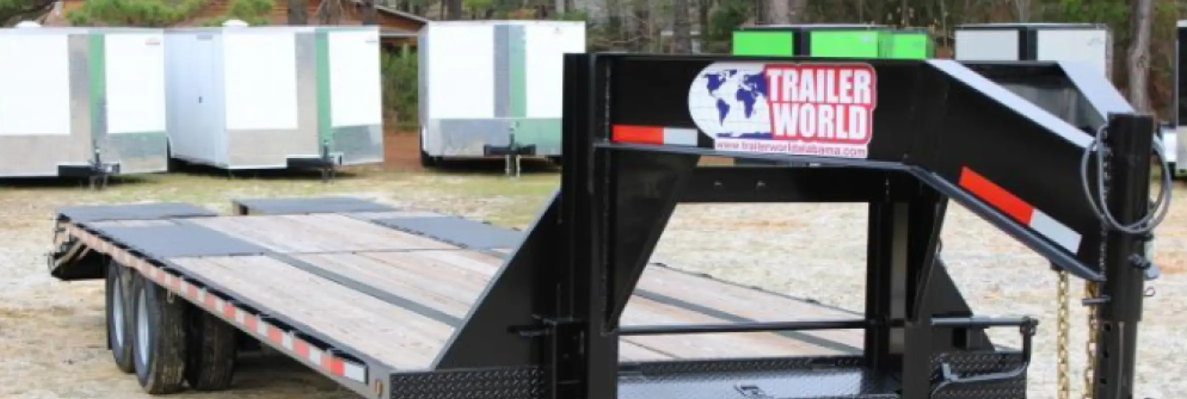 Black gooseneck flatbed trailer with wood deck displayed at Trailer World dealership lot